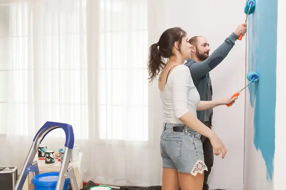 Bir kadın ve bir erkek, duvarı maviye boyarken rulo kullanıyor