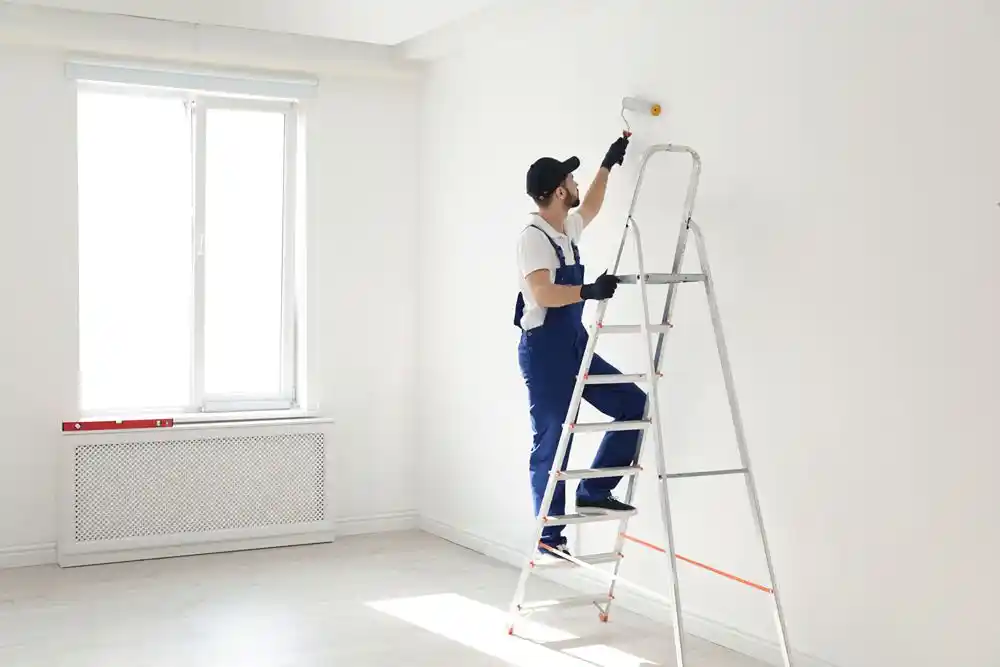 Beyaz bir odayı merdiven üzerinde duran bir işçi ruloyla boyuyor