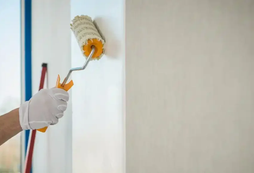 Eldivenli bir kişi, boya rulosuyla duvarı boyuyor