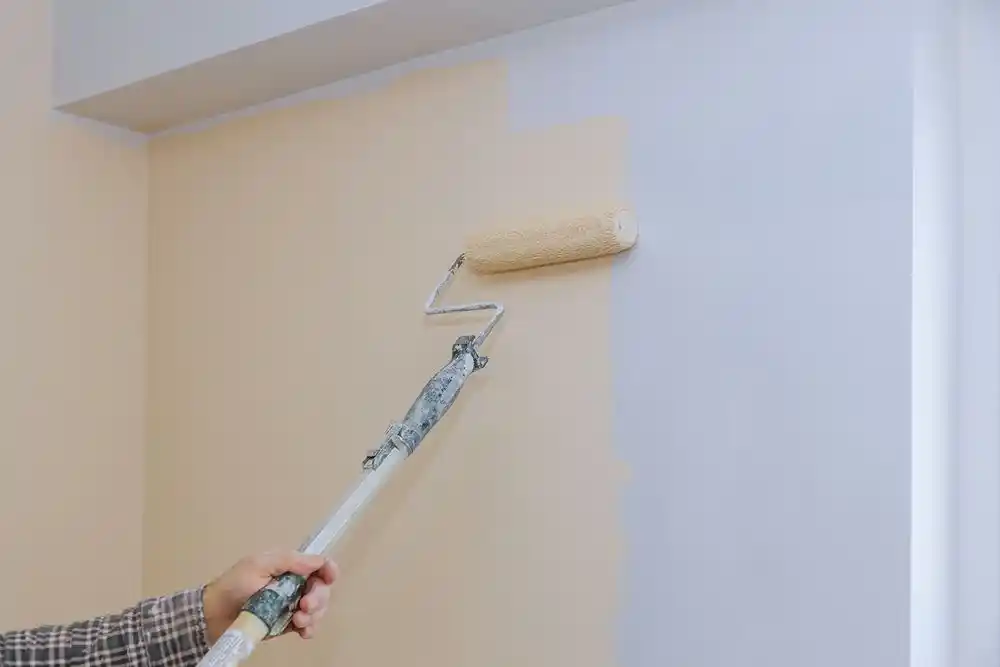 Duvarı rulo boya ile boyayan kişinin eli ve boya rulosu görülüyor