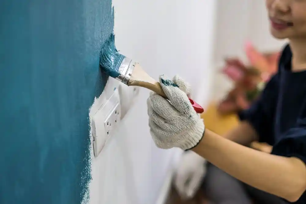Bir kişi, priz çevresindeki duvarı maviye boyamak için fırça kullanıyor